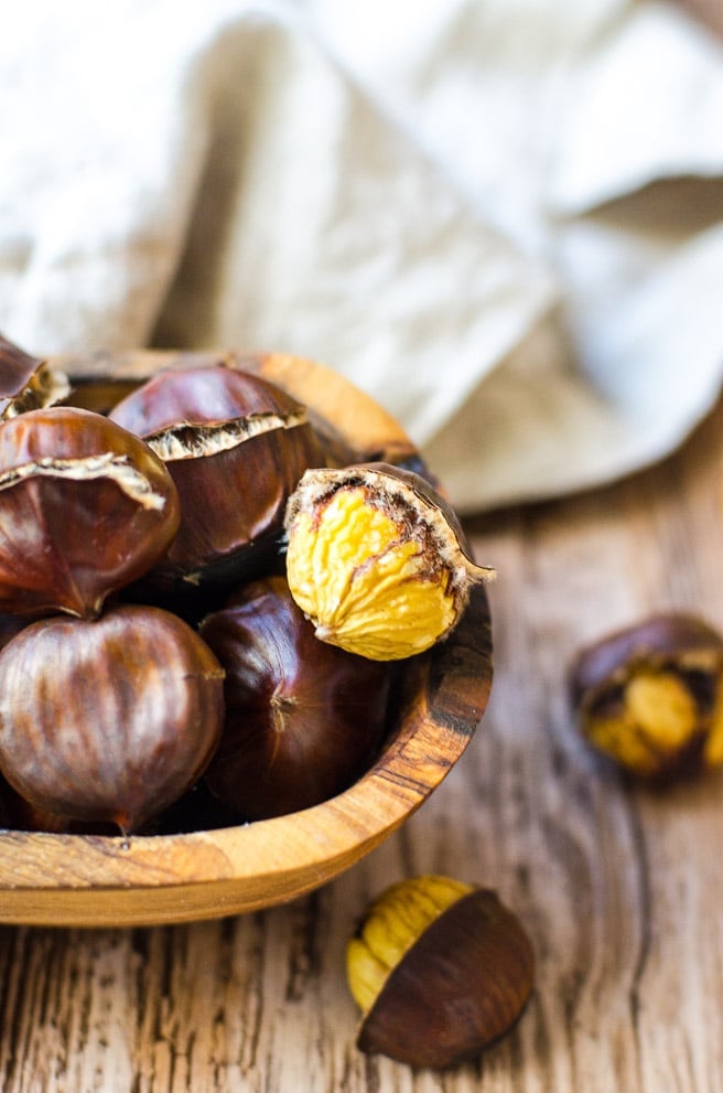 A peeled chestnut in a wooden bowl of roasted chestnuts