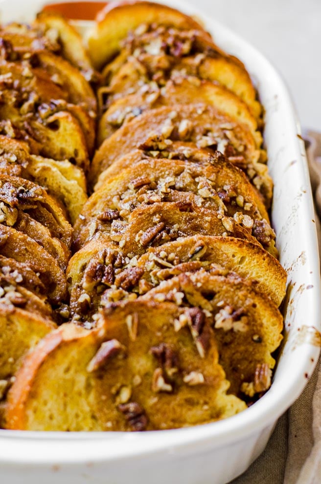 Two rows of cooked pumpkin french toast with pecan praline topping in a white baking dish.  
