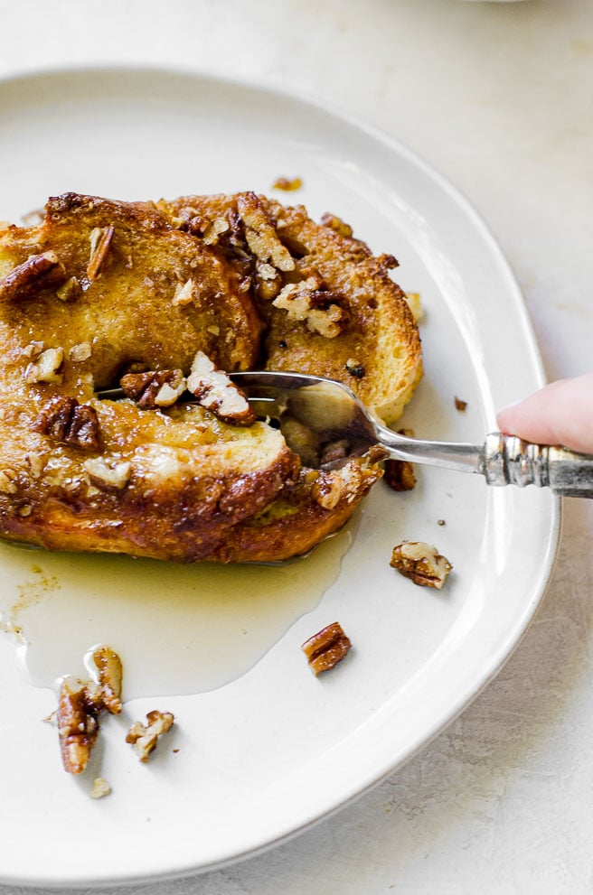 A fork cutting into a piece of french toast with syrup.