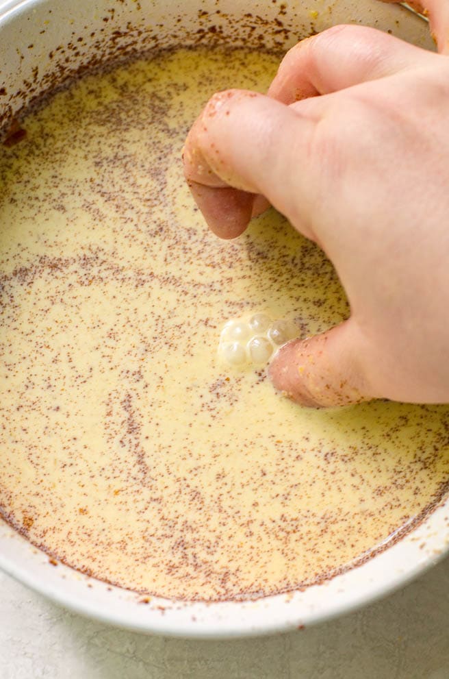 Hands submerging bread into french toast egg mixture showing the bubbles that show when it is done.