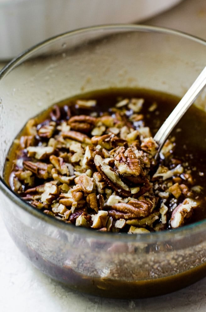 A spoon stirring chopped pecans into brown sugar for pecan praline topping.