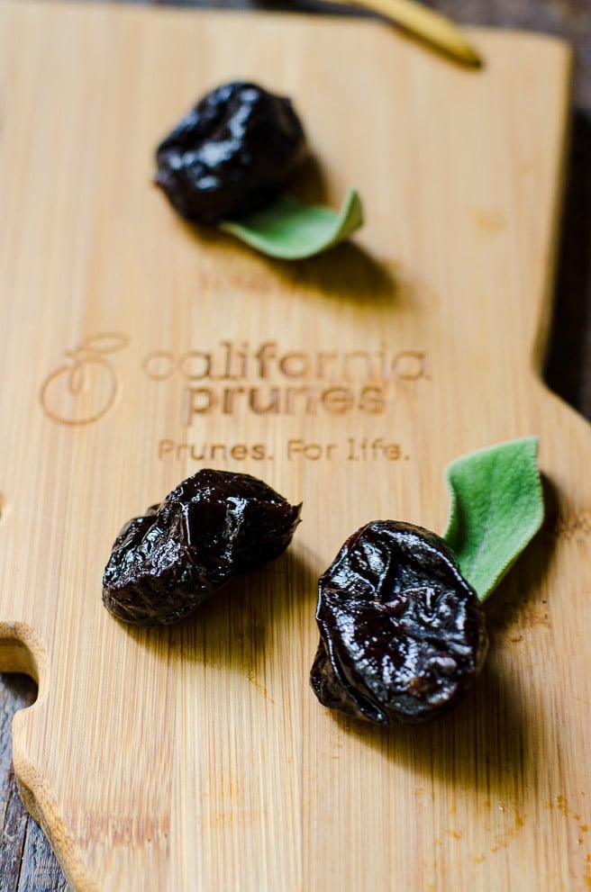A wooden cutting board with three California Prunes on it.
