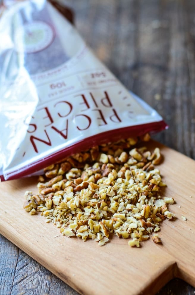 A bag pouring out pecan pieces onto a cutting board.