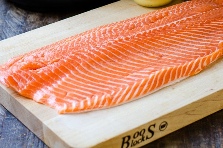 A whole salmon fillet on a wooden cutting board.