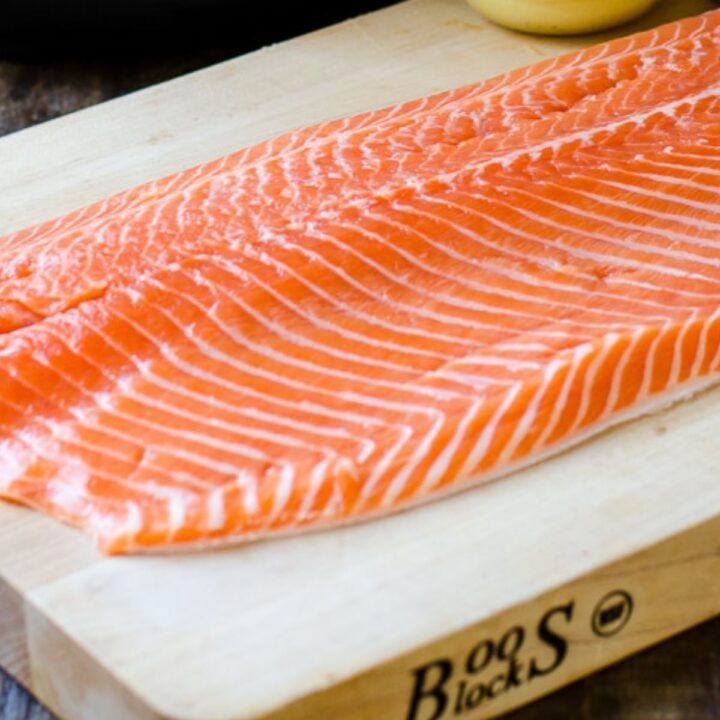 A white cutting board holding thin slices of salmon