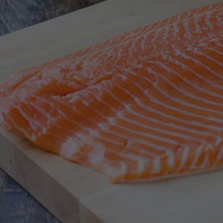 Black overlay on a side of salmon on a wooden cutting board.