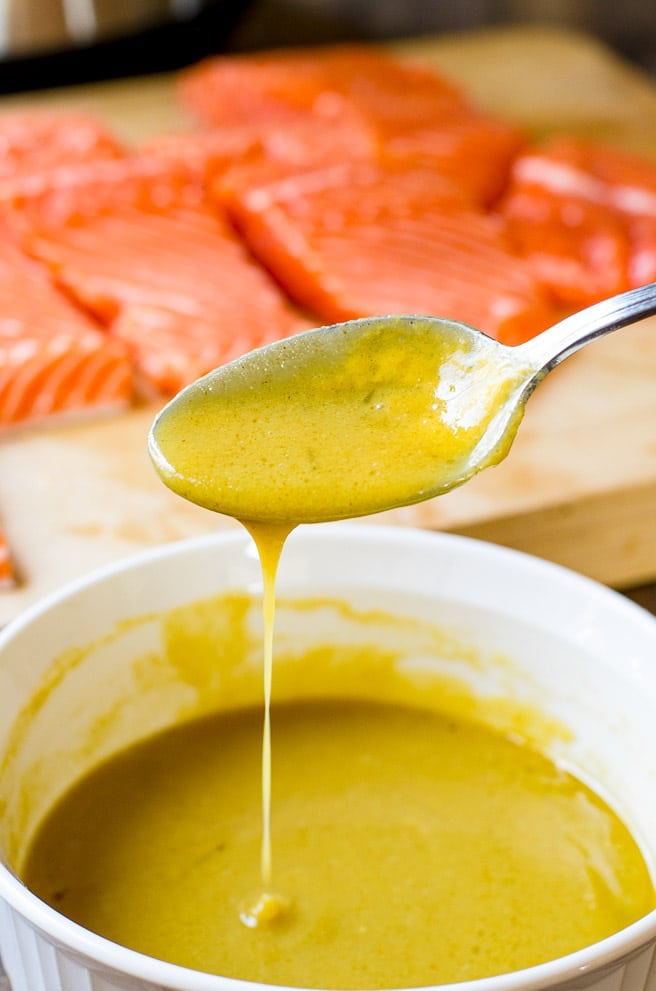 A spoon drizzling maple dijon sauce into a bowl.