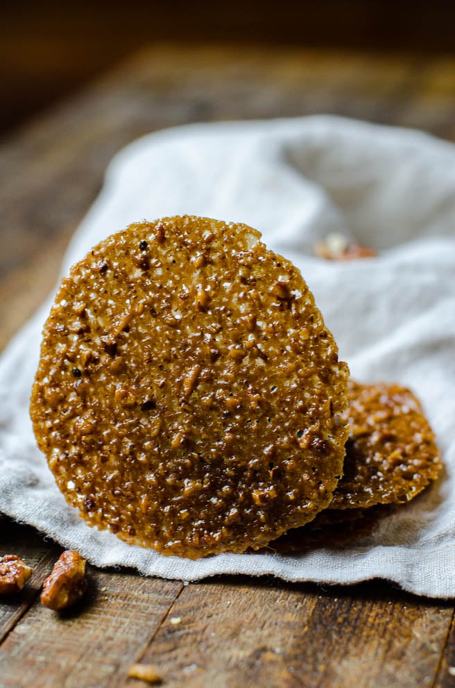 A lace cookies standing up in front of a pile of other cookies.