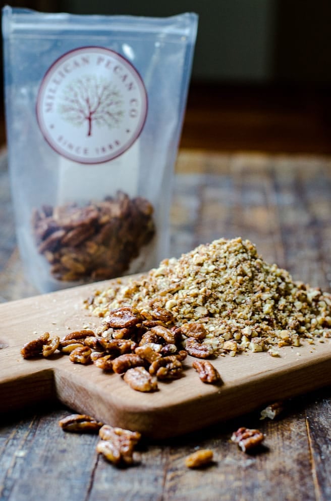 A cutting board with candied pecans next to pecans that have been ground to make pecan meal.