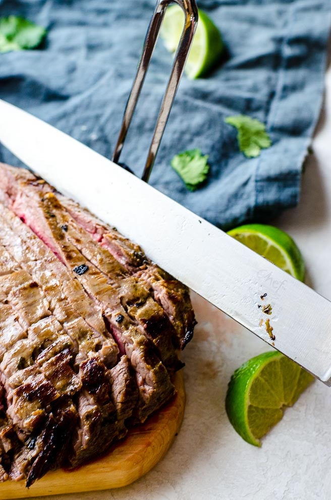 A knife slicing into flank steak showing the angle to cut to get it thin.