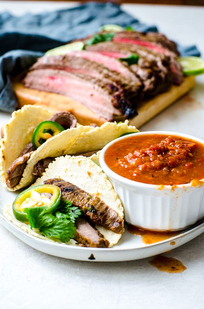 A plate of carne asada tacos next to a bowl of salsa.