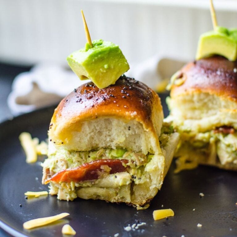 Multiple sandwiches filled with turkey and more, topped with a stick holding an avocado peice