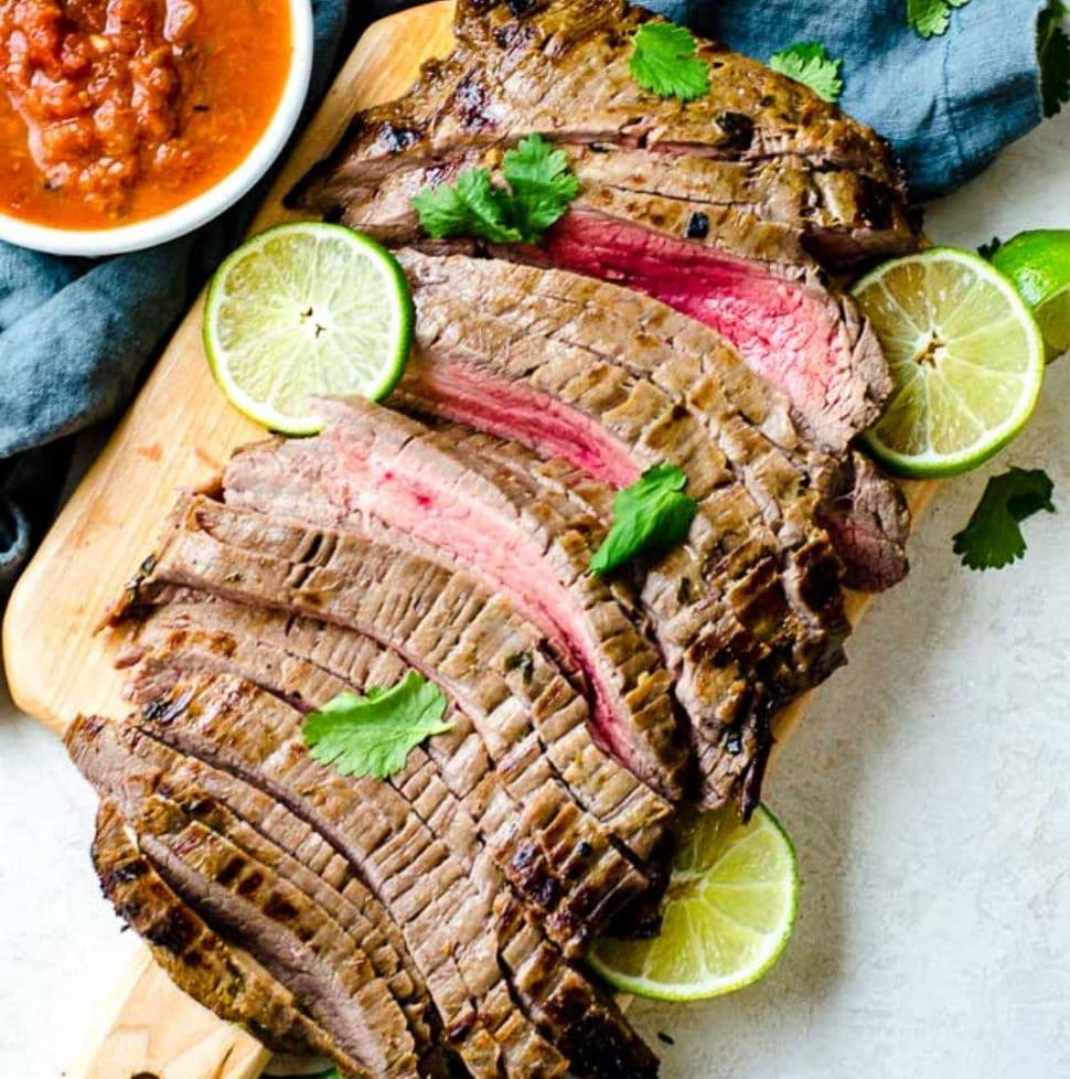 Sliced carne asada meat on a cutting board. It is cooked to medium rare.