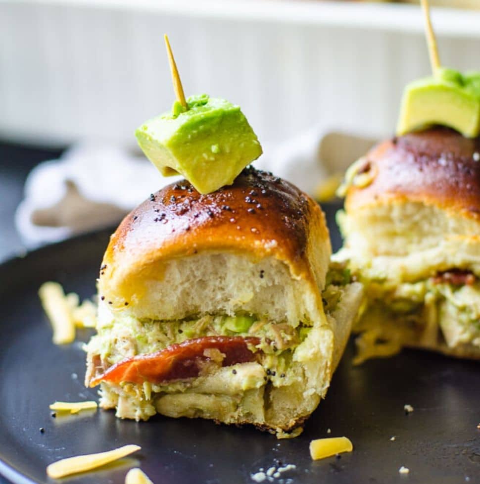 A hawaiian roll turkey slider with a toothpick in the middle on a black plate.