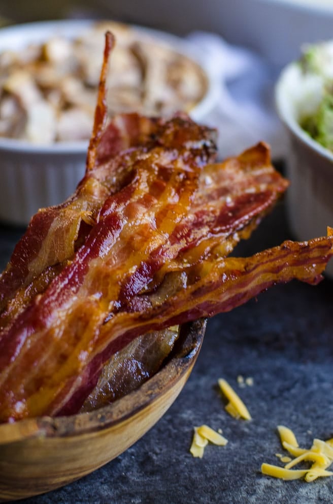 A wooden container of cooked bacon in front of other ingredients.