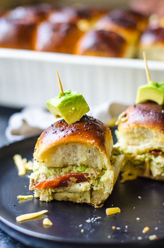 A cube of avocado garnishes turkey sliders on a black plate.