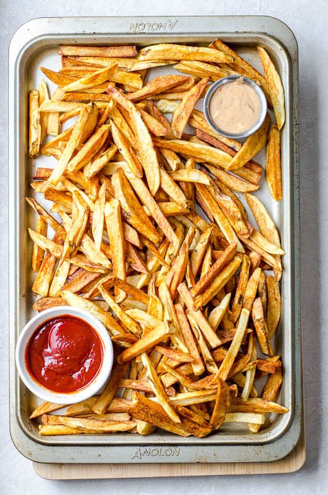 Overhead view of a baking sheet of homemade french fries and dipping sauces.