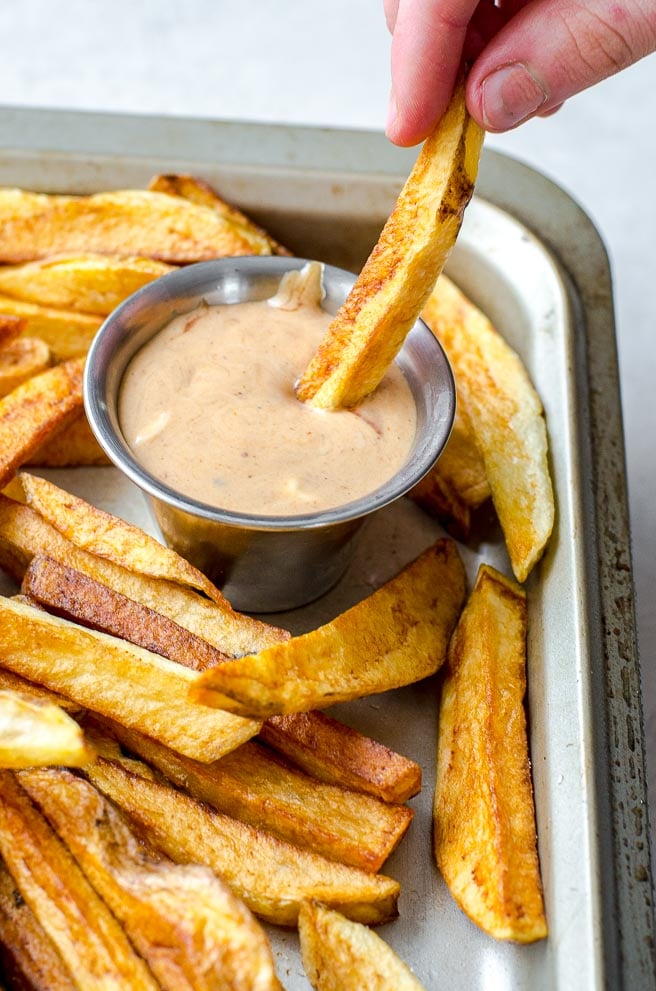 A hand dipping a french fry into fry sauce.