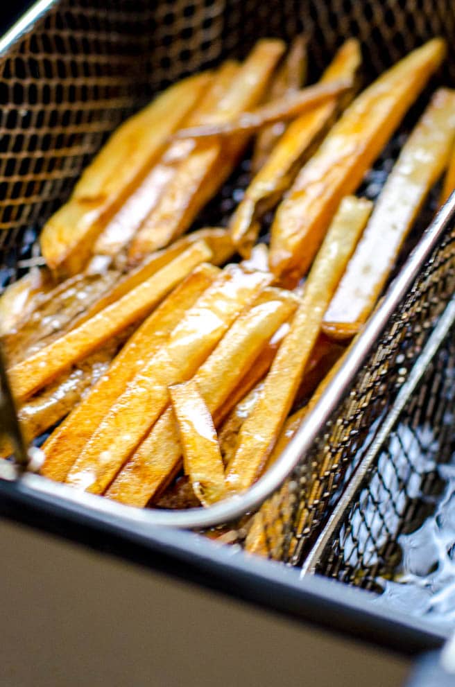 A deep fryer basket pulling out freshly fried fries.