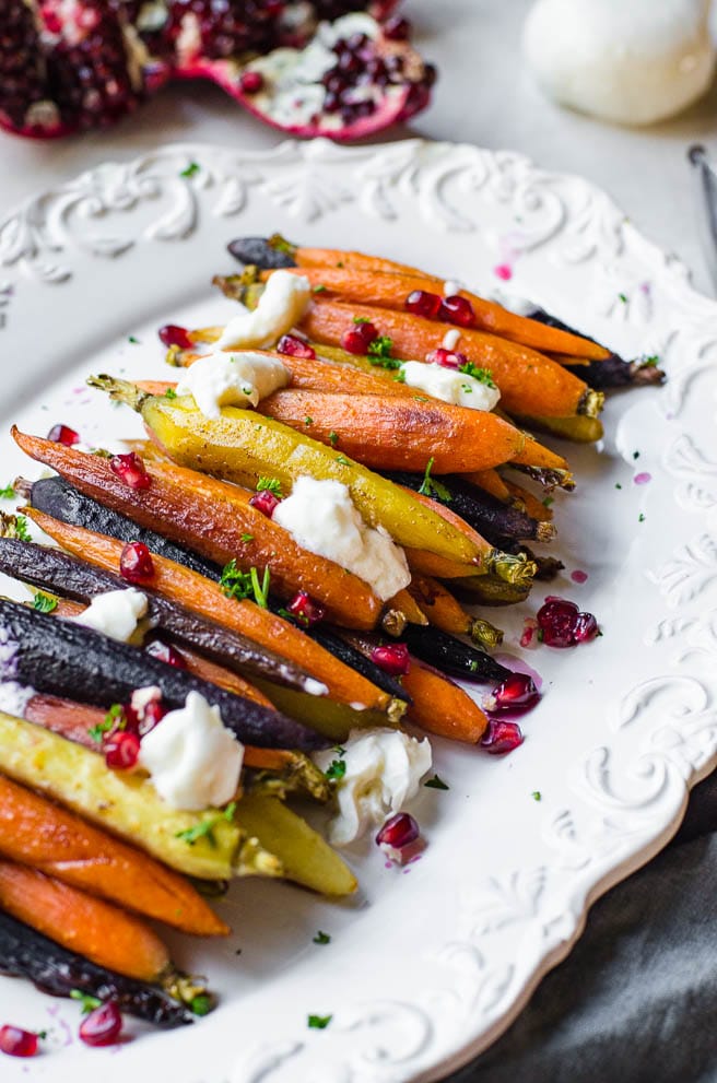 Burratta cheese and pomegranate decorating a white platter of rainbow carrots.