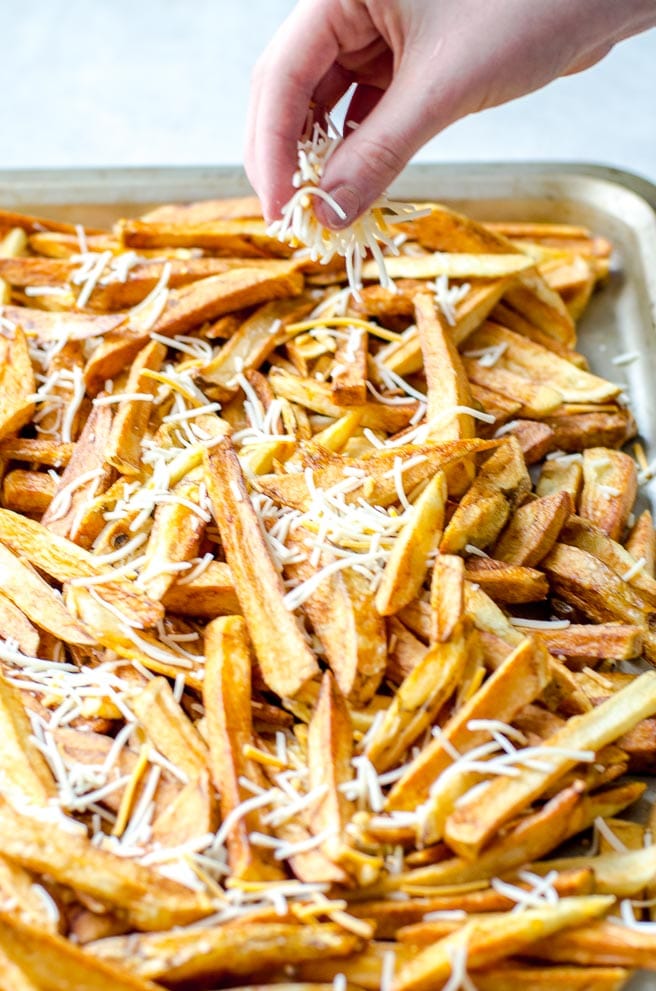 A hand sprinkling cheese onto french fries.