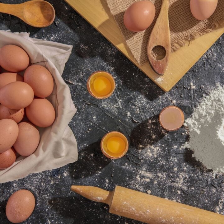 A picture of a basket holding brown eggs, along with a rolling pin surrounded by flour