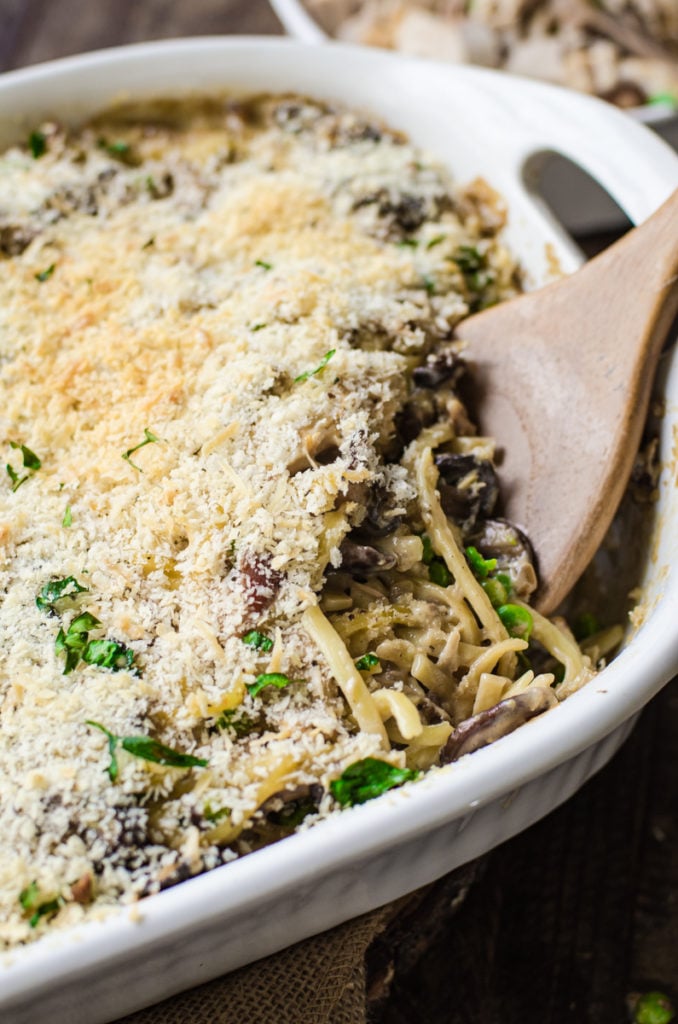 A wooden serving spoon scooping turkey tetrazzini out of a casserole dish.