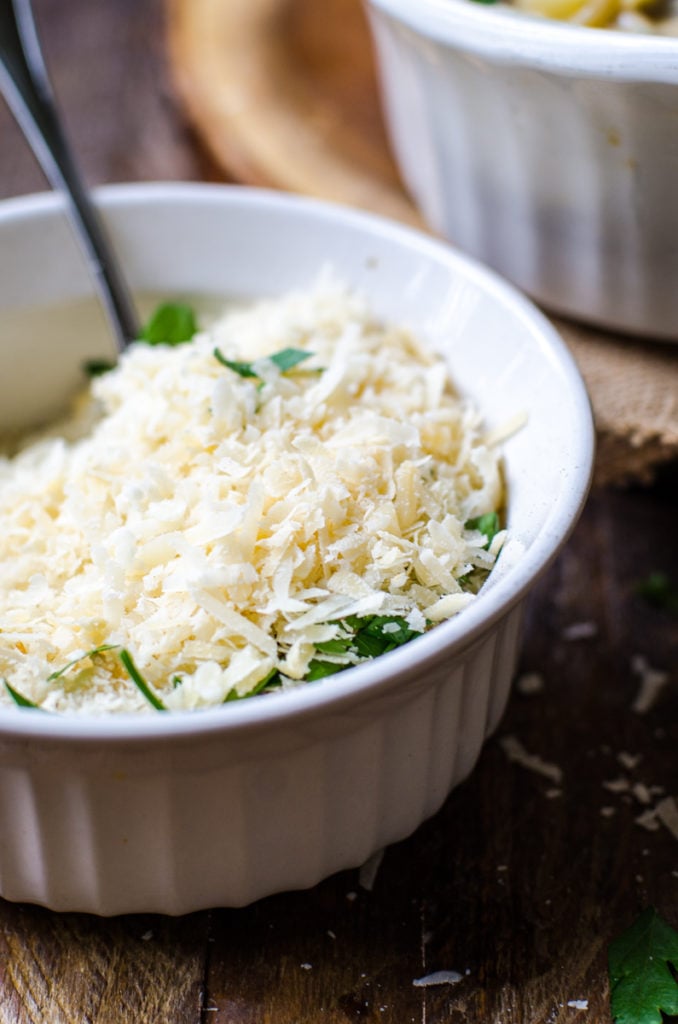 A white bowl of shredded cheese and parsley.