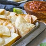 Homemade tortilla chips on a pan next to salsa.