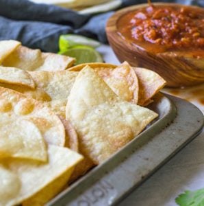 Homemade tortilla chips on a pan next to salsa.