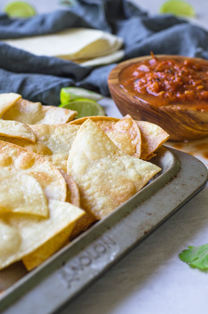 A sheet pan of tortilla chips by limes and salsa.