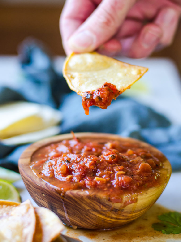 A hand holding a tortilla chip pulling salsa out of a bowl