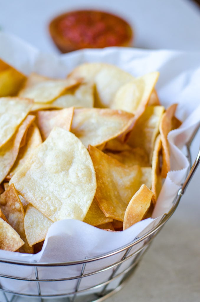 A basket of homemade tortilla chips in front of a bowl of salsa.