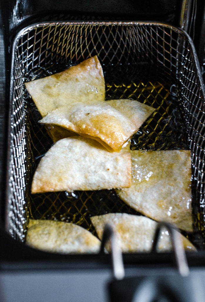 Tortillas frying in a deep fryer basket.