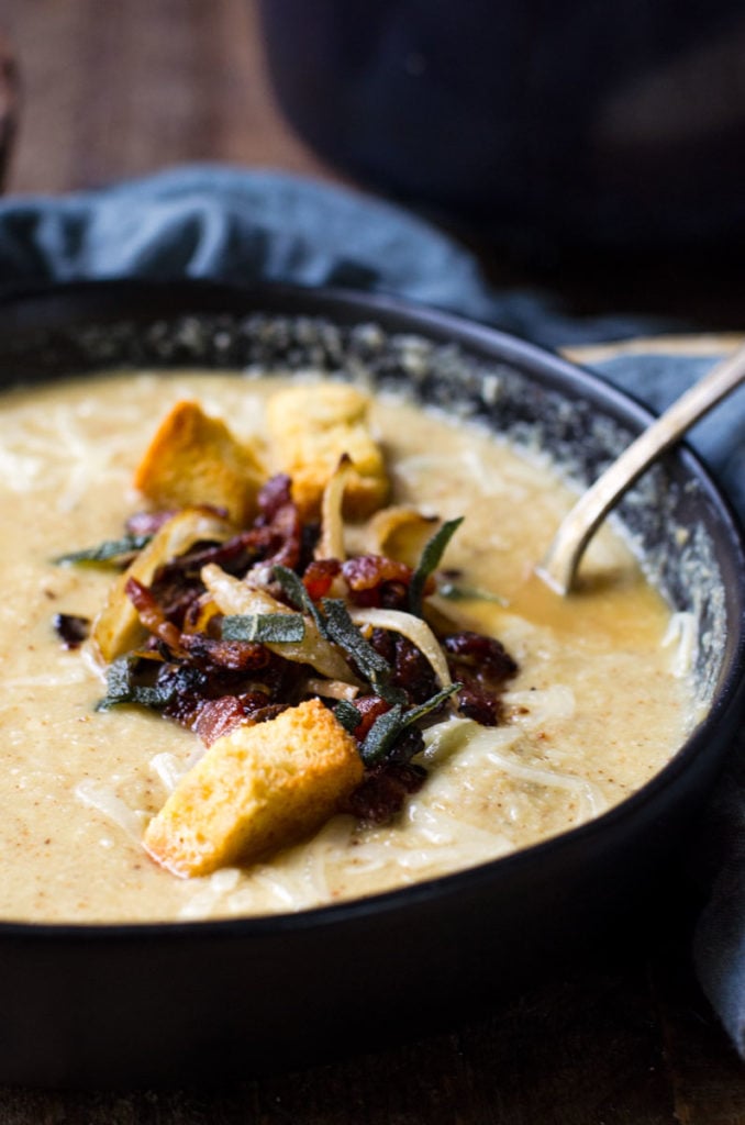 A black bowl of roasted cauliflower soup with bacon and croutons.