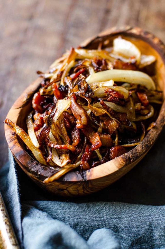 A wooden container of caramelized onions and cooked bacon.