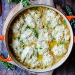 Overhead view of a pot of cooked turkey and dumplings garnished with rosemary.