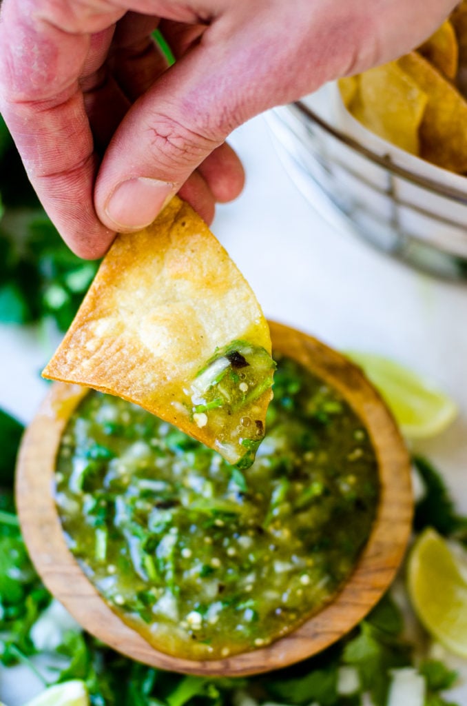 A hand dipping a chip into green salsa.