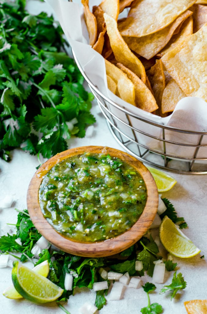 A wooden bowl of salsa next to a basket of tortilla chips.