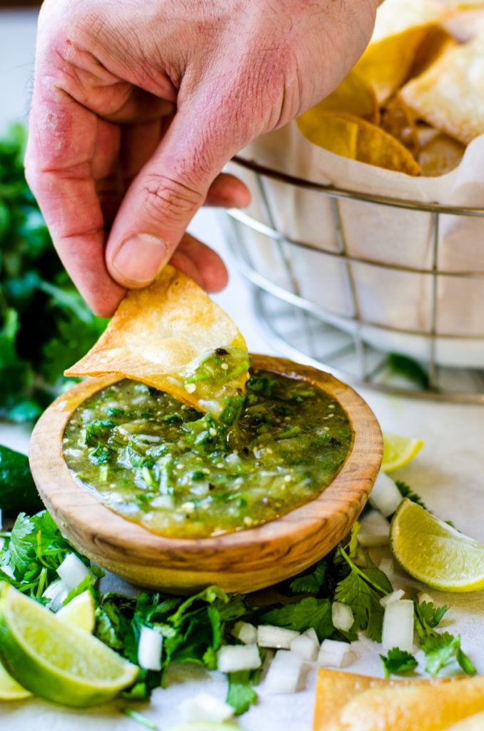 A hand dipping chips into salsa.