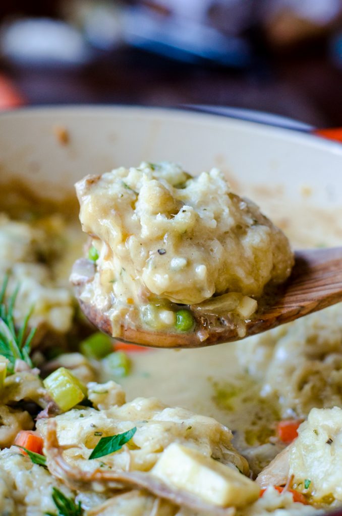 A wooden spoon lifting turkey and dumplings out of a pot.