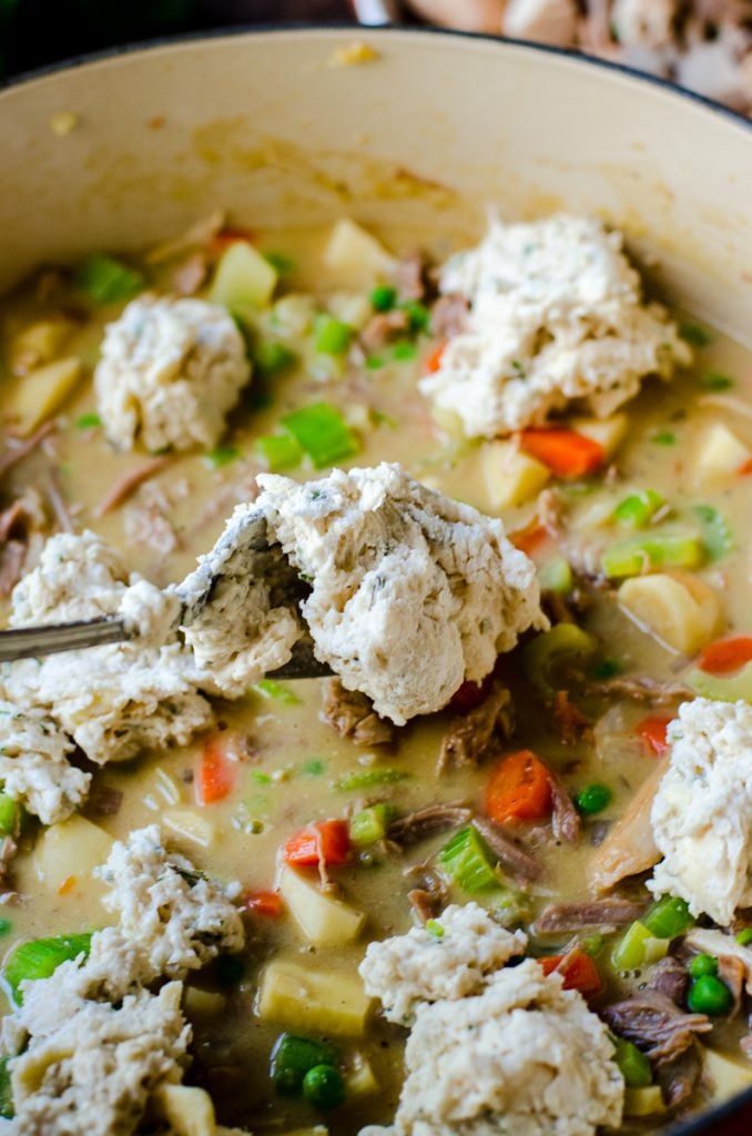 A spoon dropping dumplings on top of stew.