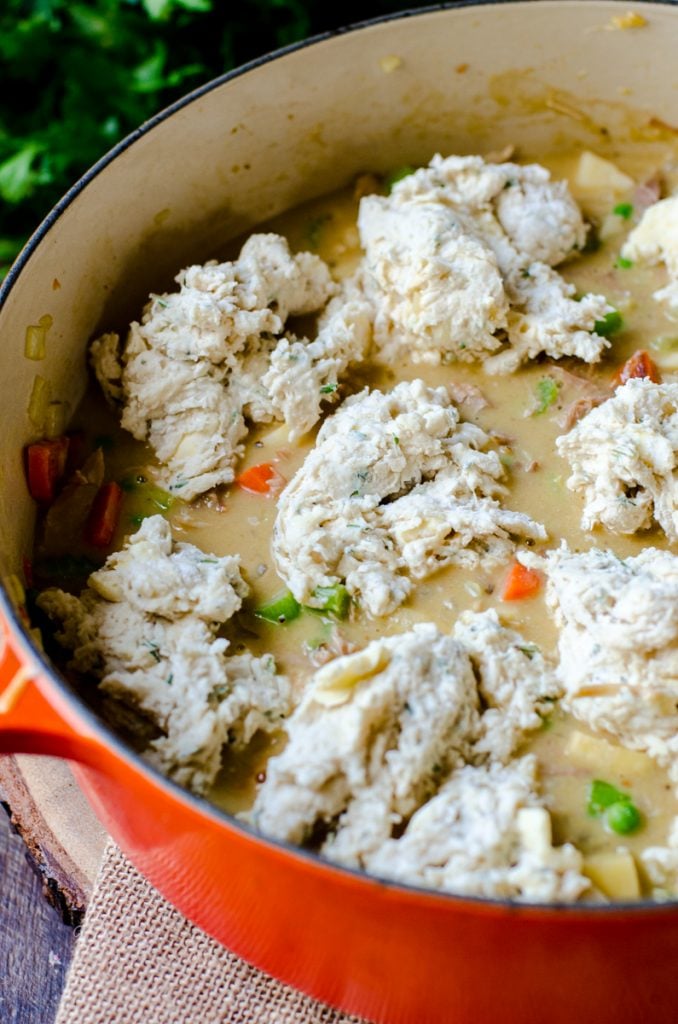 A dutch oven with stew and raw dumplings.