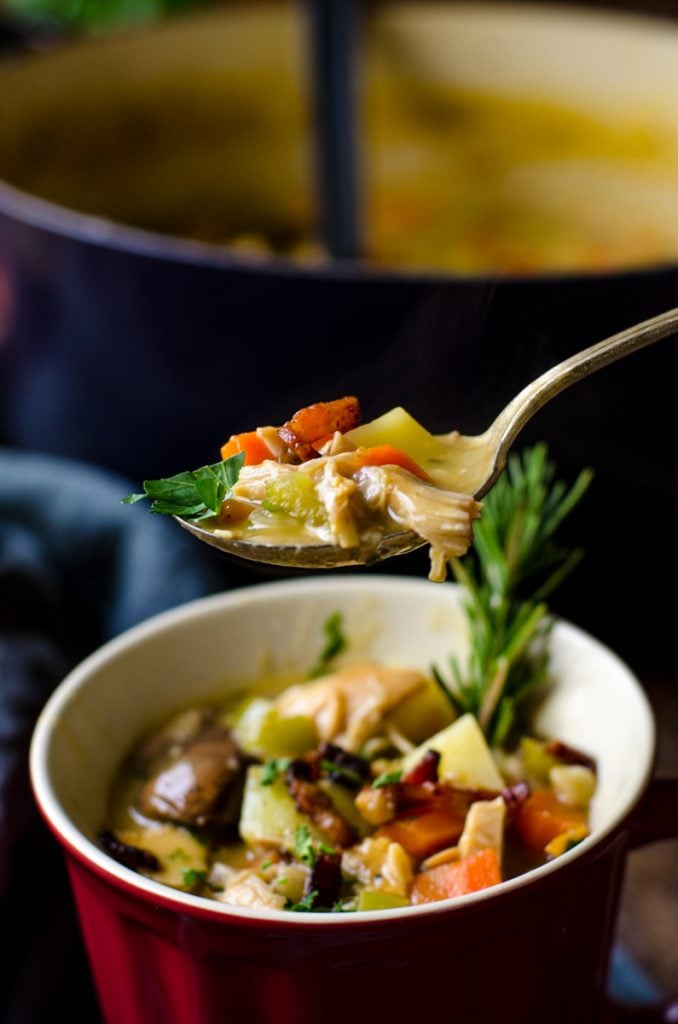 A spoon lifting leftover turkey soup out of a bowl.