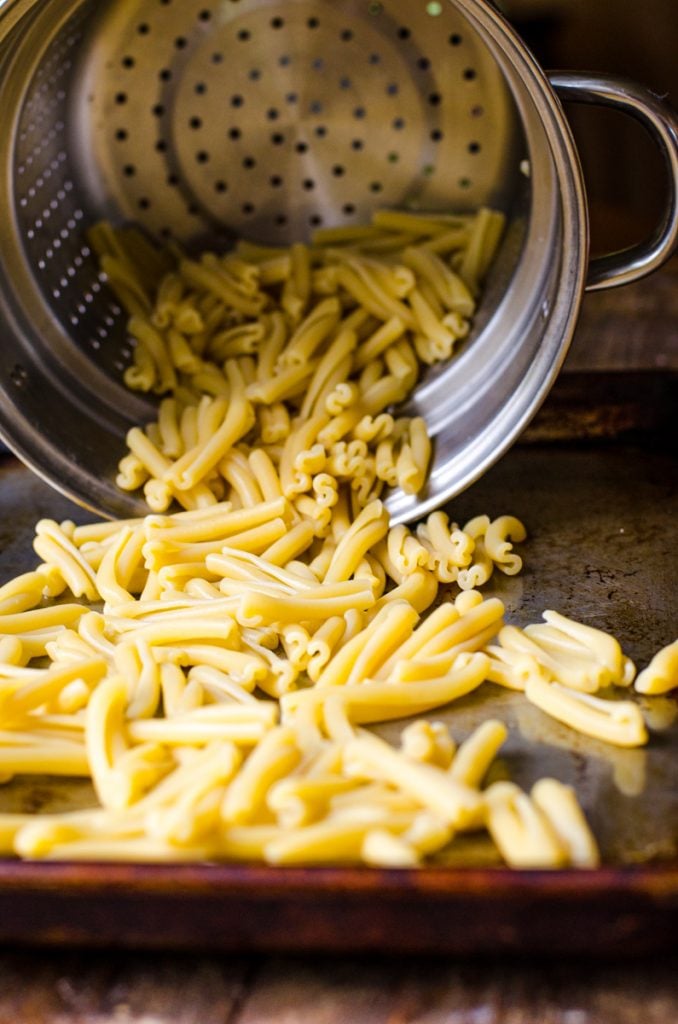 A pasta strainer pouring out casarecce noodles onto a baking sheet for cooling.