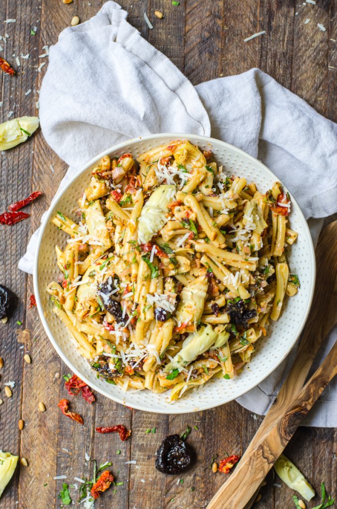 Serving tongs next to a bowl of sun-dried tomato pasta salad