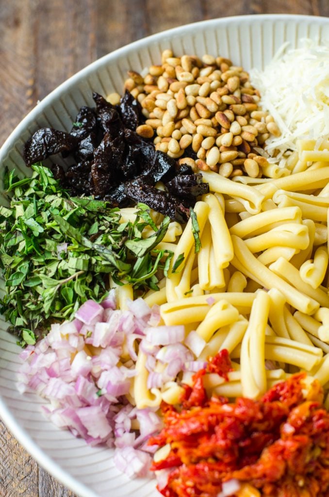 Ingredients for pasta salad in a bowl separated by type. Focus is on California Prunes.