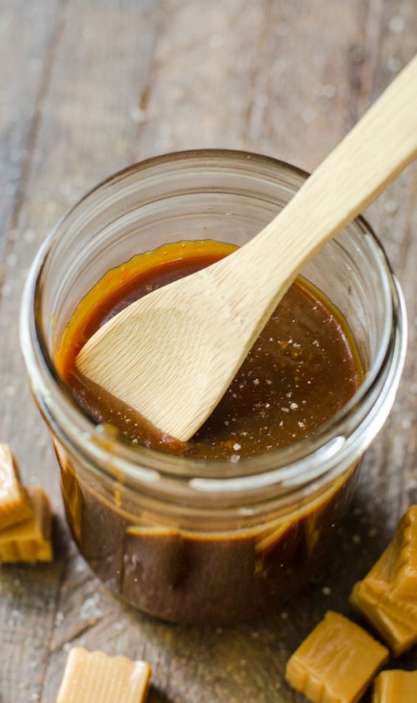 A wooden spoon scooping up caramel sauce from a jar.