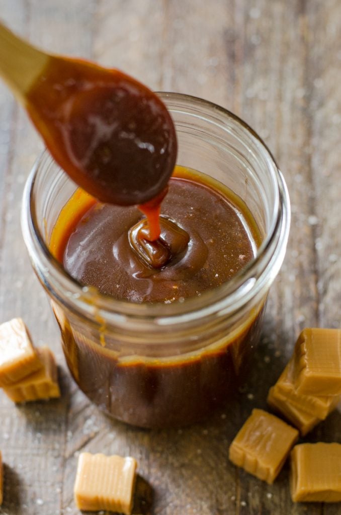 A spoon drizzling caramel sauce showing the consistency of the sauce.
