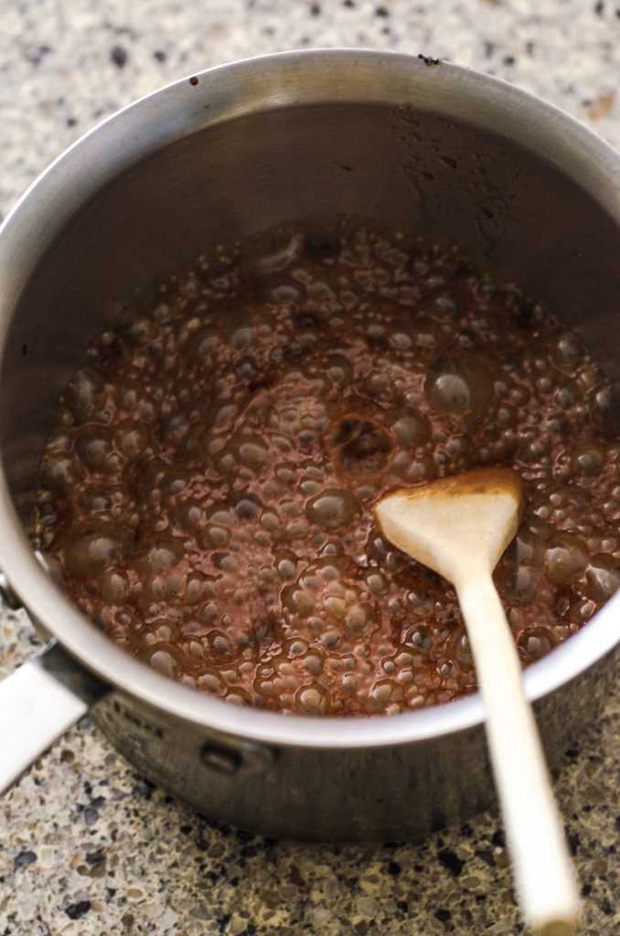 A frothing and foaming pot of caramel being stirred with a wooden spoon.